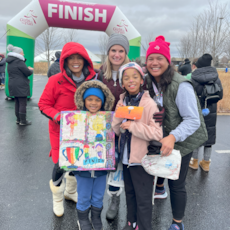 Girls on the Run participant is surrounded by family and supporters holding a cheer sign