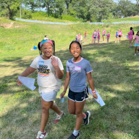 Two Girls on the Run participants smile at the camera while running at an outdoor practice